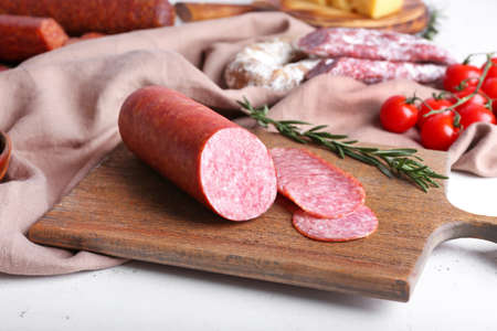 Board with tasty salami on light background