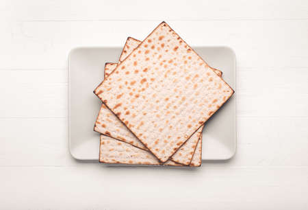 Plate with Jewish flatbread matza for Passover on white wooden background