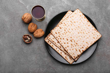 Plate with Jewish flatbread matza for Passover, cup of wine and walnuts on gray backgroundの写真素材