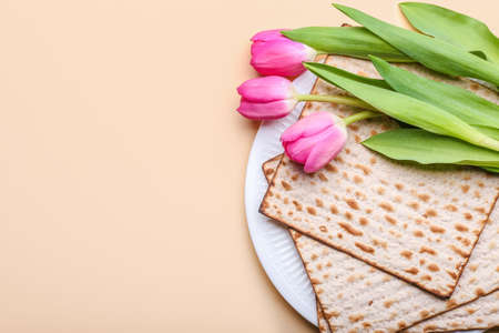 Plate with Jewish flatbread matza for Passover and flowers on color background