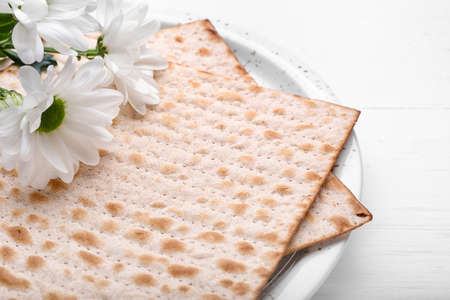 Plate with Jewish flatbread matza for Passover and flowers on white background, closeup