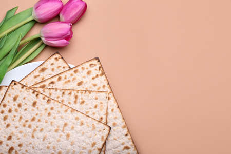 Plate with Jewish flatbread matza for Passover and flowers on color background