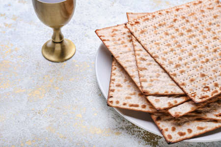 Plate with Jewish flatbread matza for Passover and cup of wine on light background