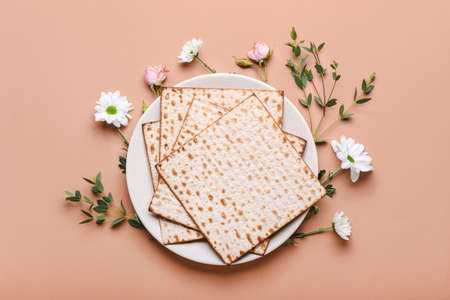 Plate with Jewish flatbread matza for Passover and flowers on color background