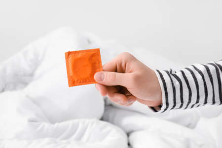 Hand of man with condom in bedroomの写真素材