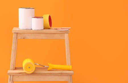 Cans of paints, tape and roller on ladder near color wall
