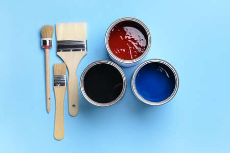 Cans of paints and brushes on color background