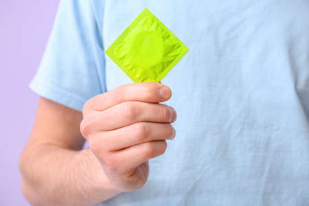 Man with condom in package on color background, closeupの写真素材