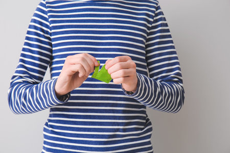 Man opening package of condom on gray background, closeup
