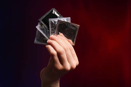 Male hand with condoms on dark backgroundの写真素材