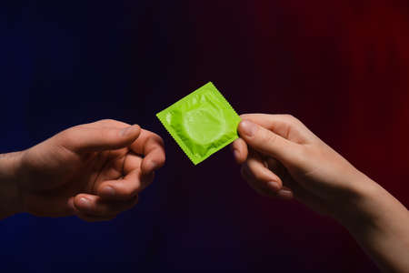 Hands of couple with condom on dark background