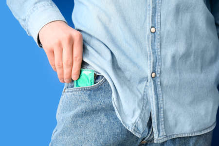 Man putting condom into pocket of jeans on color background, closeupの写真素材