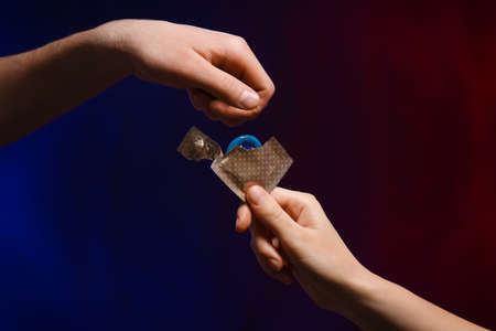 Hands of couple with condom on dark backgroundの写真素材