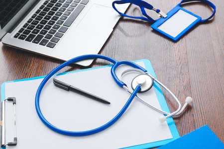 Stethoscope, clipboard, pen, laptop and badge on wooden backgroundの写真素材