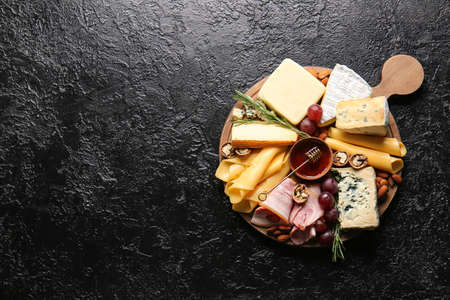 Board with tasty cheese, honey and snacks on dark backgroundの写真素材