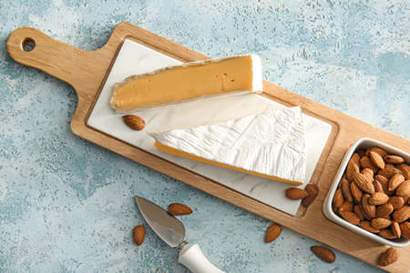 Board with tasty cheese and almond nuts on color background