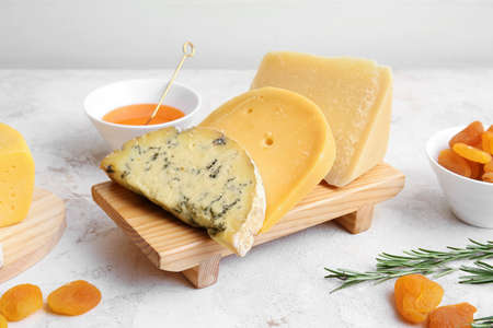 Different types of cheese, dried apricots and honey on light background, closeup