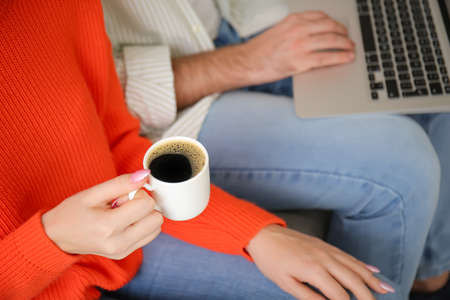 Young couple with laptop drinking hot coffee at home, closeupの写真素材