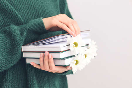 Woman holding books with fresh flowers on light background, closeupの写真素材