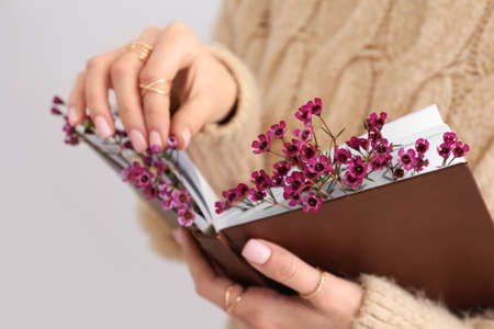 Woman holding book with fresh flowers, closeup