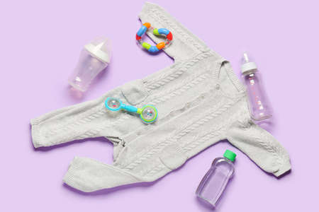 Stylish baby clothes with toys and bottles on color backgroundの写真素材