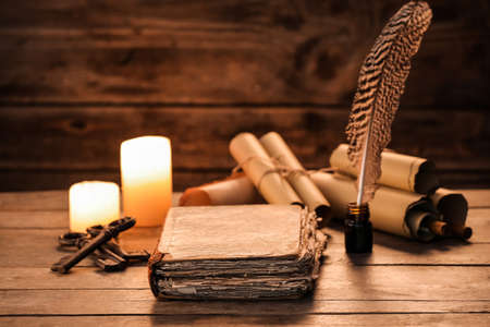 Old book with scrolls, feather, keys and candles on wooden backgroundの写真素材