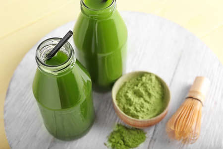 Tray with bottles of matcha tea, powder and chasen on color wooden background, closeup