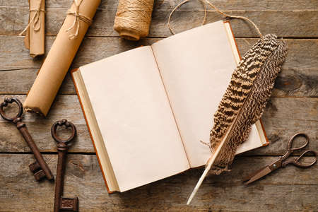 Open old book with scrolls, feather and keys on wooden background