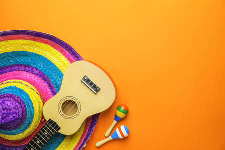 Mexican sombrero, guitar and maracas on color background