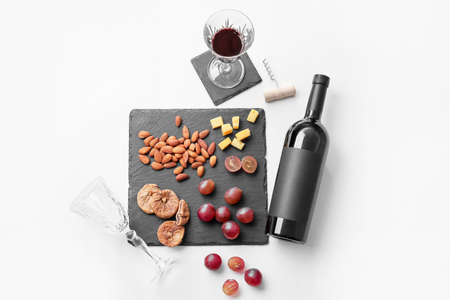 Composition with bottle of wine, glasses and snacks on white background