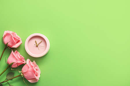 Alarm clock with rose flowers on color background