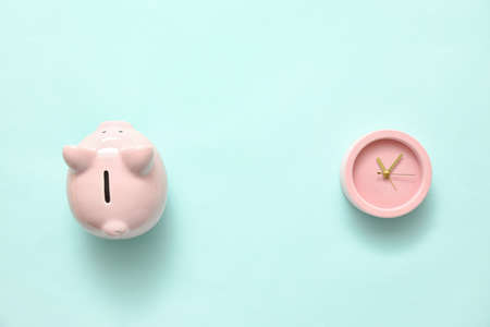 Alarm clock with piggy bank on color background