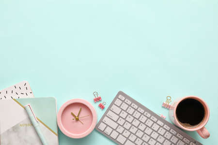 Alarm clock with office supplies, cup of coffee and computer keyboard on color backgroundの写真素材