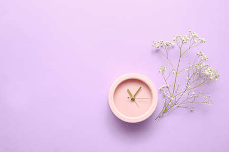 Alarm clock with flowers on color background