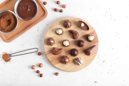Board with tasty candies, liquid chocolate and cacao powder on white background