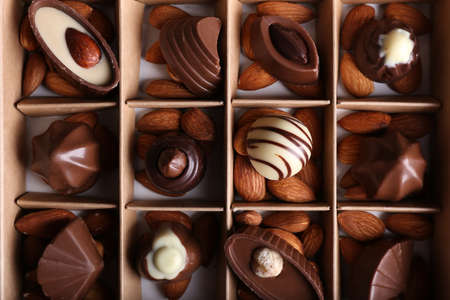 Box with tasty chocolate candies and almond nuts, top view