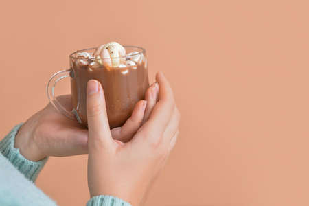 Hands of young woman with hot cocoa on color background