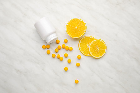Bottle with vitamin C pills and lemon slices on light background