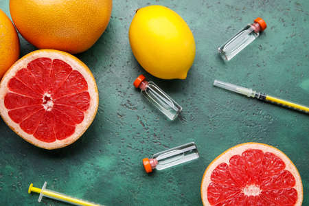 Bottles with vitamin C and citrus fruits on color background