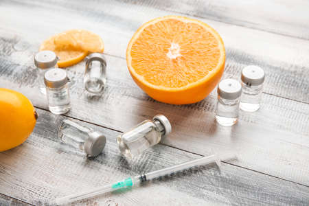 Ampules with vitamin C, syringe and citrus fruits on wooden background