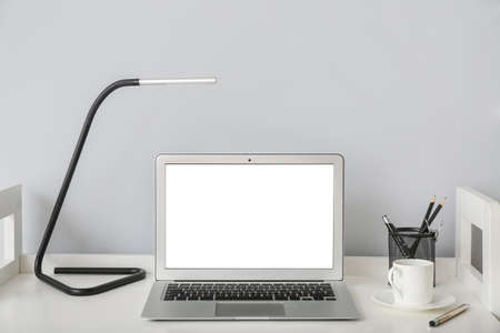 Table with laptop and lamp near light wall in room
