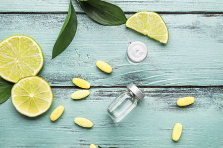 Bottles with vitamin C, pills and lime slices on color wooden backgroundの写真素材