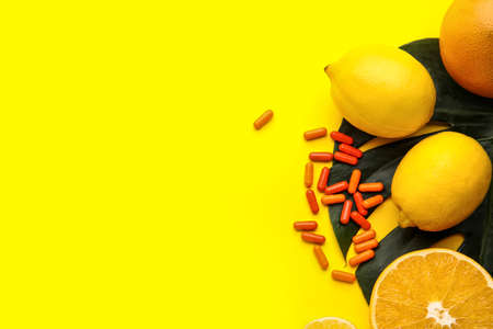 Vitamin C pills and citrus fruits on color background
