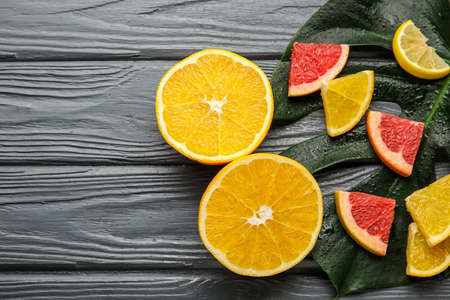 Ripe citrus fruits and tropical leaf on dark wooden background