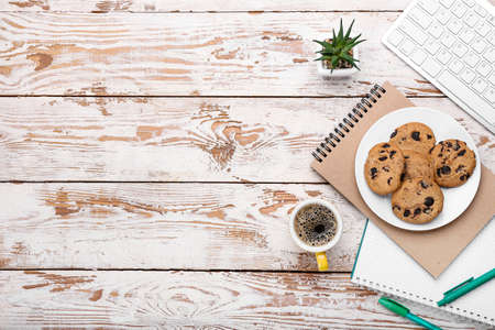 Cup of coffee, keyboard, cookies and stationery on light wooden backgroundの写真素材