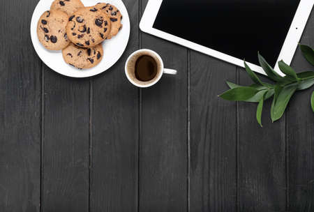 Cup of coffee, tablet computer and cookies on dark wooden backgroundの写真素材