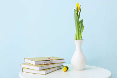 Vase with fresh tulip flowers, jewelry and books on table against color backgroundの写真素材