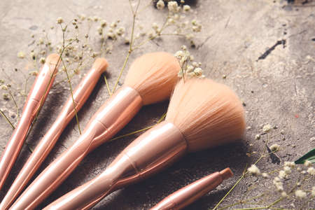 Makeup brushes and flowers on gray background