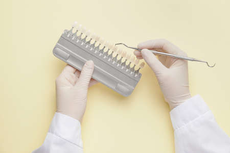 Dentist with instrument and teeth samples on color backgroundの写真素材