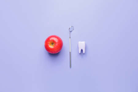 Dentist's mirror, plastic tooth and apple on color backgroundの写真素材